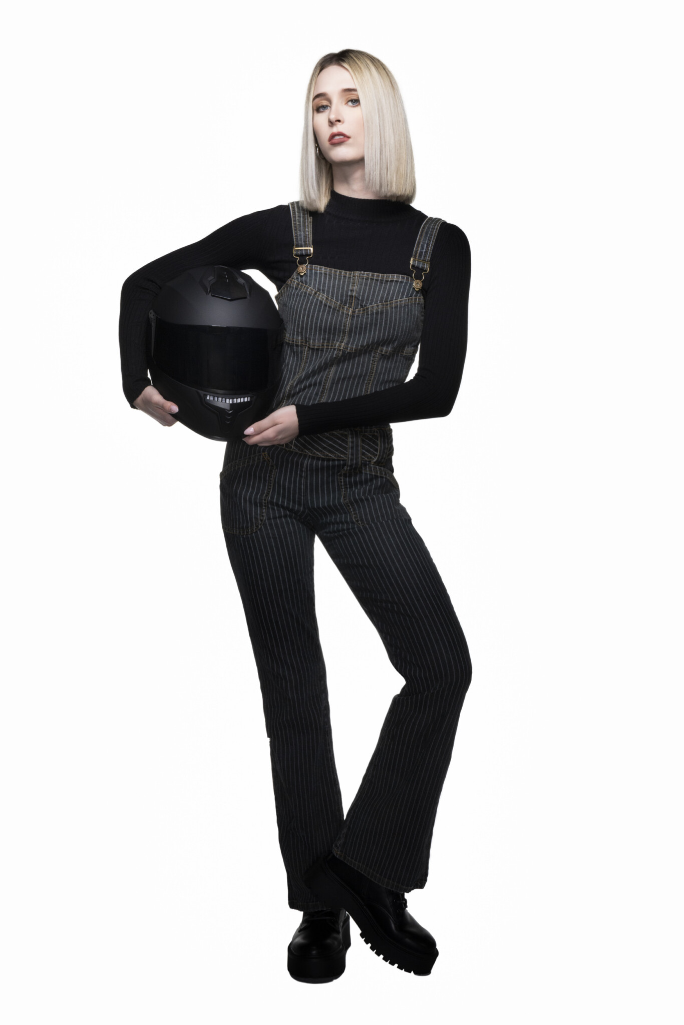 Full-length wide aperture studio portrait of a blonde woman in all black holding a biker helmet with white background