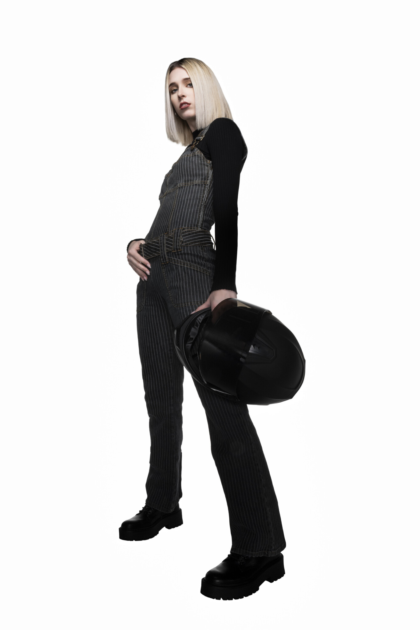 Full-length wide aperture studio portrait of a blonde woman in all black holding a biker helmet with white background