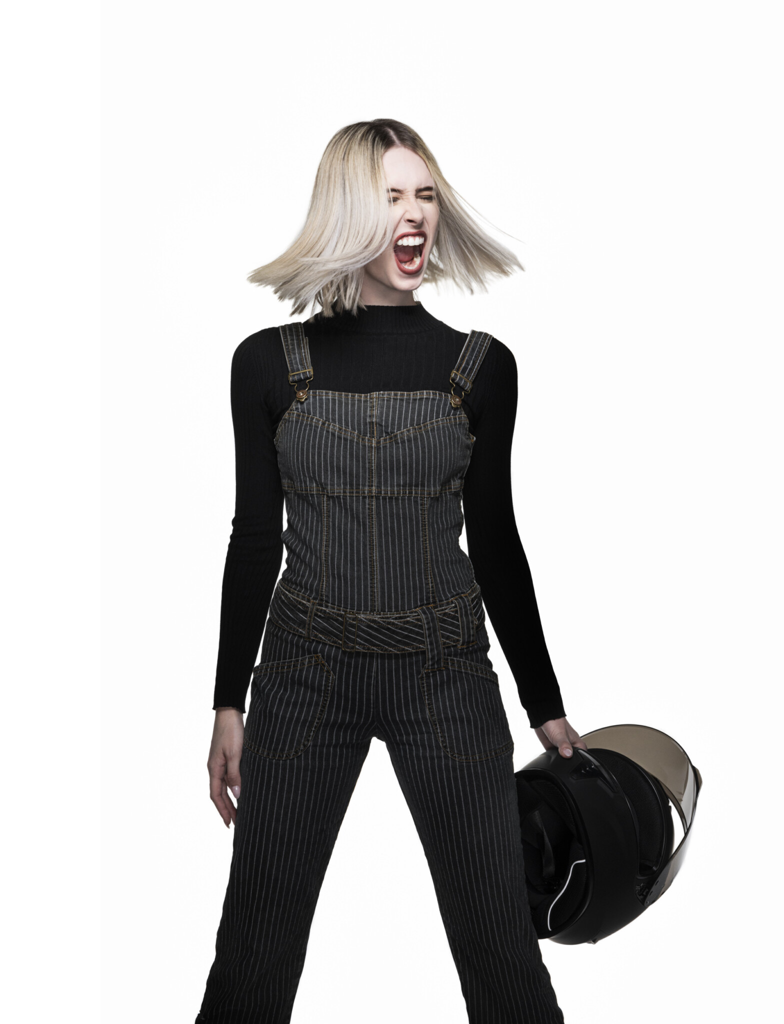 Full-length wide aperture studio portrait of a blonde woman in all black holding a biker helmet and screaming with a white background