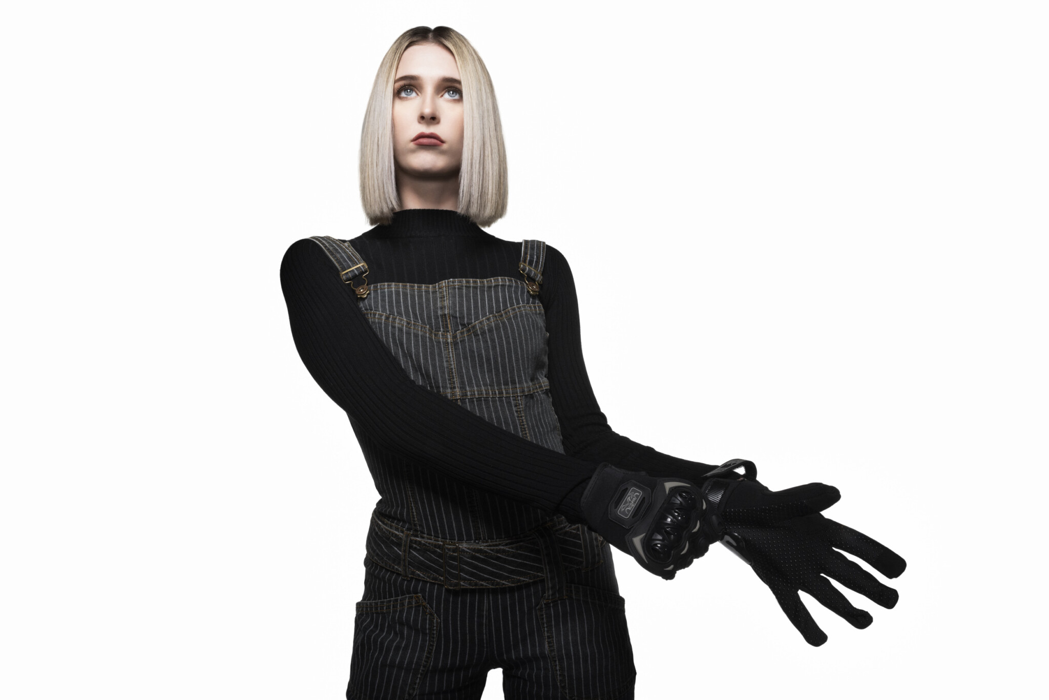 Wide aperture shot of Blonde woman in all black putting on a glove on a white background